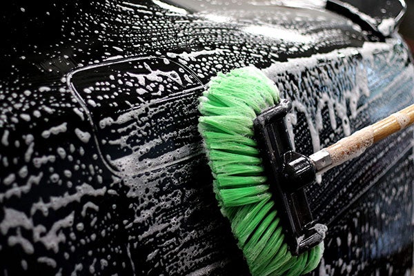 scrub brush cleaning side of black car